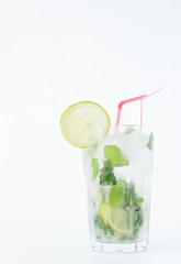 Mojito cocktail in a transparent glass with ice. Recipe for exotic drinks with mint, lime and white rum. Glass with a cocktail on a white background in the rays of the sun.