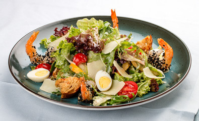Fresh caesar salad on white bowl with parmesan cheese and shrimps. In a decorative plate
