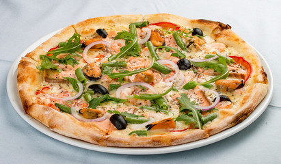 Delicious hot pizza with salmon, mussels, olives, tomatoes and various spices. On white background