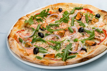 Delicious hot pizza with salmon, mussels, olives, tomatoes and various spices. On white background