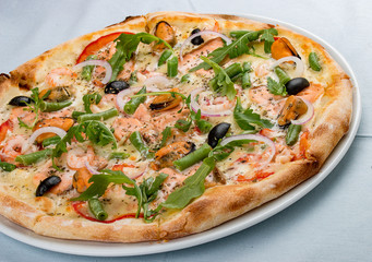 Delicious hot pizza with salmon, mussels, olives, tomatoes and various spices. On white background