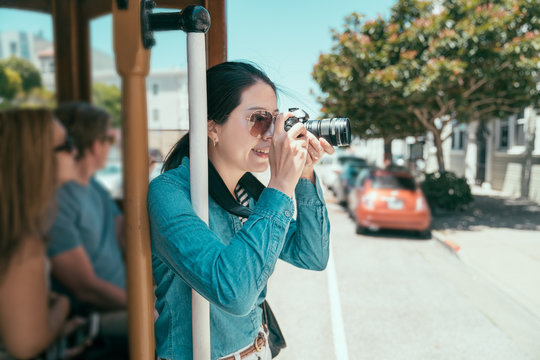 travel woman taking photo in city during day time while having summer trip in san francisco. young girl passenger on cable car holding hand rail and using camera photographing sunny urban view.