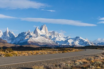 Beautiful Fitz Roy and Cerro Torre peak snow mountain in the morning blue sky with golden yellow grass beside the asphalt road route 40 road from El Calafate to El Chalten, south Patagonia, Argentina - obrazy, fototapety, plakaty