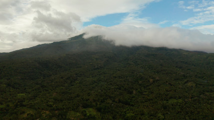 Obraz na płótnie Canvas Aerial view of tops of the mountains covered with clouds in the evening Camiguin, Philippines. Mountain landscape on tropical island with mountain peaks covered with forest. Slopes of mountains with