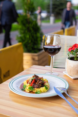 Comfort meal on a summer terrace: russian beef stroganoff with gravy, mashed potatoes, parsley and caramelized onion with a glass of red wine