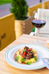 Comfort meal on a summer terrace: russian beef stroganoff with gravy, mashed potatoes, parsley and caramelized onion with a glass of red wine