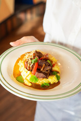 Waiter is serving classic beef stroganoff with gravy, mashed potatoes and caramelized onion