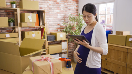 Obraz na płótnie Canvas Small business owner woman checking new order from customer on digital pad shopping online at office. young pregnant motherhood lady one hand touching expecting baby in belly another holding tablet.