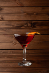 Red alcoholic cocktail in a shot glass on a totally wooden background: homemade bitter berry tincture with a slice of orange peel