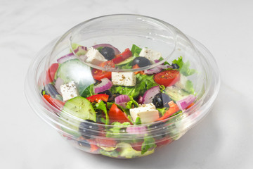 Fresh greek salad in a plastic package to take away for lunch on white marble background