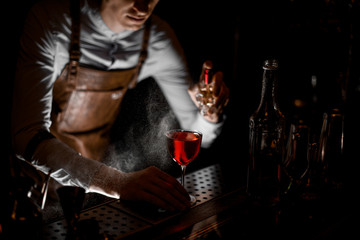 Male bartender spraying on the red alcoholic cocktail