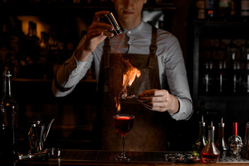 Bartender add spices for a decor in the fire above a delicious red cocktail in the glass