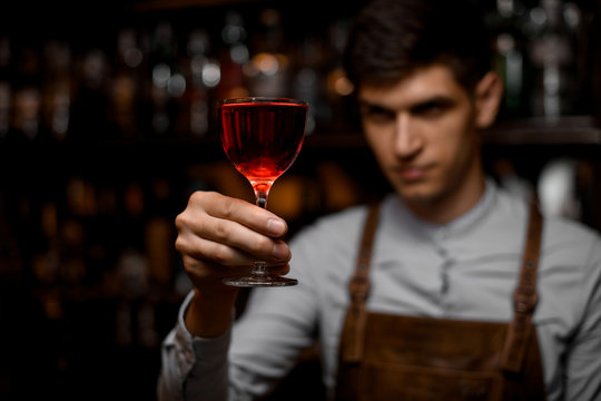 Attractive bartender serving a red alcoholic cocktail in the glass