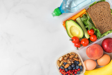 healthy lunch boxes with sandwich, vegetables, nuts, berries, banana, eggs, avocado, peaches and water