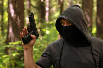 Man in hood with the pistol in the forest.
