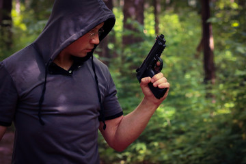 Man in hood with the pistol in the forest.
