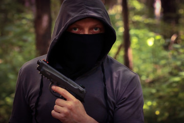 Man in hood with the pistol in the forest.