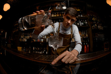 Fisheye shot professional male bartender pouring a cocktail from the measuring cup to the glass