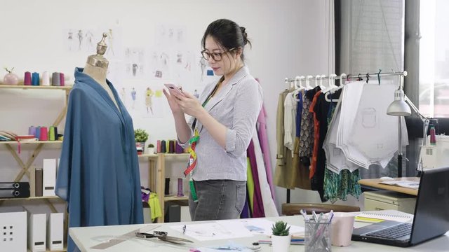 Fashion designer woman last check on smart phone information of customer order photograph. young professional female worker holding cellphone with new collection on mannequin model dummy in studio.