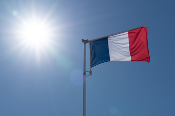 Flag of France waving over blue sky and large sun