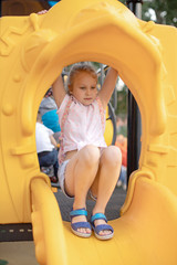Little girl sitting on the tube slide at the kids playground. Cute child playing outdoor