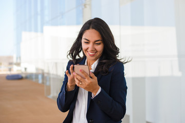 Smiling businesswoman messaging via smartphone. Beautiful happy young woman in formal wear using...