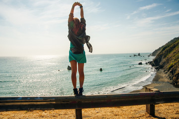 back woman traveler standing on the road in big sur mountain with blue sky. California Coast, USA