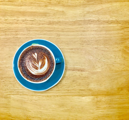 Hot dark chocolate in blue cup on wooden table background. Art of milk foam drawing like white leaf on dark brown melt chocolate top view.