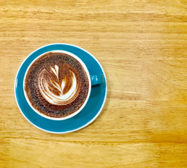 Hot dark chocolate in blue cup on wooden table background. Art of milk foam drawing like white leaf on dark brown melt chocolate top view.