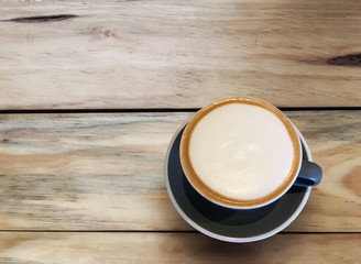 Hot cappuccino coffee in blue cup on wooden table background. Art of milk foam circle shape with copy space on brown melt coffee top view