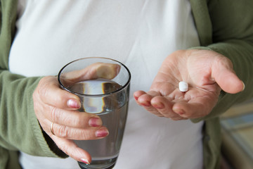 senior woman's hand closeup with medicines and glass of water