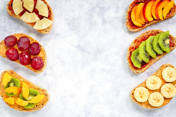 Healthy breakfast toasts with peanut butter, strawberry jam, banana, grapes, peach, kiwi, pineapple, nuts. Copy space