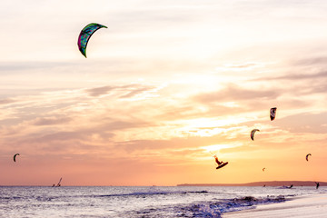 extreme group of professional kiters slide waves, jumps air on black sea with sail wing in hands led wind an sunset, onlookers photographers seagull on shore. village of annunciation. backlit, toned