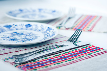 Table setting for dinner: white and blue plates, a fork, a knife on a woven cloth napkin with an embroidered pattern,  traditional handmade in Ukraine.