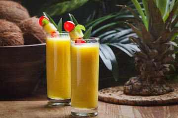 Tropical  cocktail pineapple  in a glasses, garnished with  cherries maraschino on wooden  table .