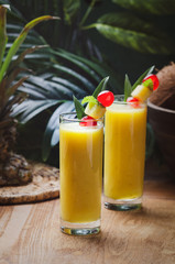Tropical  cocktail pineapple  in a glasses, garnished with  cherries maraschino on wooden  table .