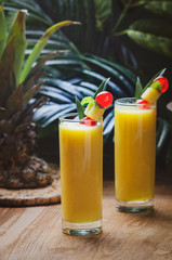 Tropical  cocktail pineapple  in a glasses, garnished with  cherries maraschino on wooden  table .