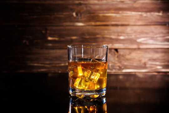 Glasss of whiskey with ice cubes on wooden background
