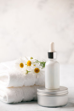 Spa and wellness setting. Composition with chamomile flowers and cosmetic bottle of essential oil serum and cream in zero waste pacage on white background