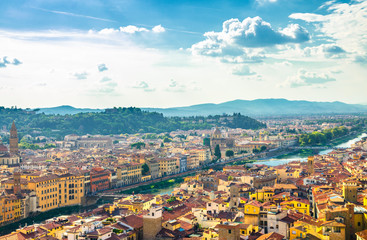Top aerial panoramic view of Florence city historical centre, bridges over Arno river, buildings houses with orange red tiled roofs, blue sky white clouds background, Tuscany, Italy