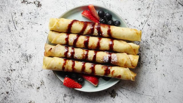 Plate of delicious crepes roll with fresh fruits and chocolate