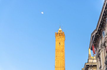 Obraz premium Top of Garisenda medieval tower of Bologna and moon with blue sky background in early evening, Emilia-Romagna, Italy