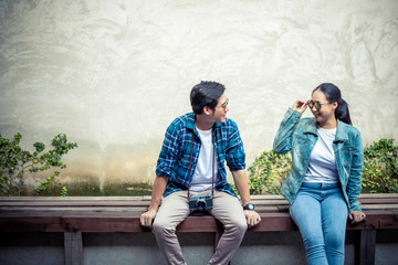 Asian couple who are starting to create love and relationship sitting on a bench in a park.