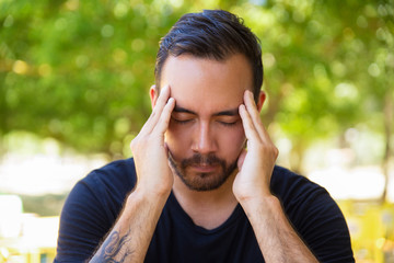 Stressed young man rubbing temples. Young bearded man with closed eyes suffering from headache outdoor. Stress concept