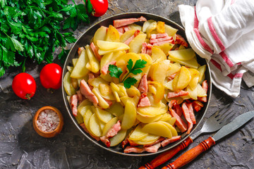 Fried potatoes with meat in a pan on the background of the stone. Quick lunch or dinner from potatoes.