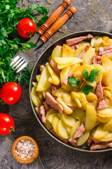 Fried potatoes with meat in a pan on the background of the stone. Quick lunch or dinner from potatoes.