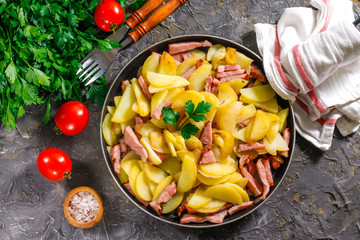 Fried potatoes with meat in a pan on the background of the stone. Quick lunch or dinner from potatoes.