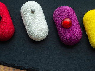 Selection of colorful dessert pastry sweet mini cakes on slate and wooden background