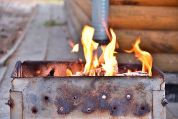Metal portable barbecue with burning firewood and red flames. Barbecue outdoor.  Bonfire for cooking meat. Fire and coal in the grill. Brazier equipment. BBQ picnic. Flaming wood with fire and ashes