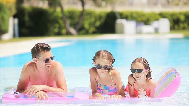 Happy family of four in outdoors swimming pool